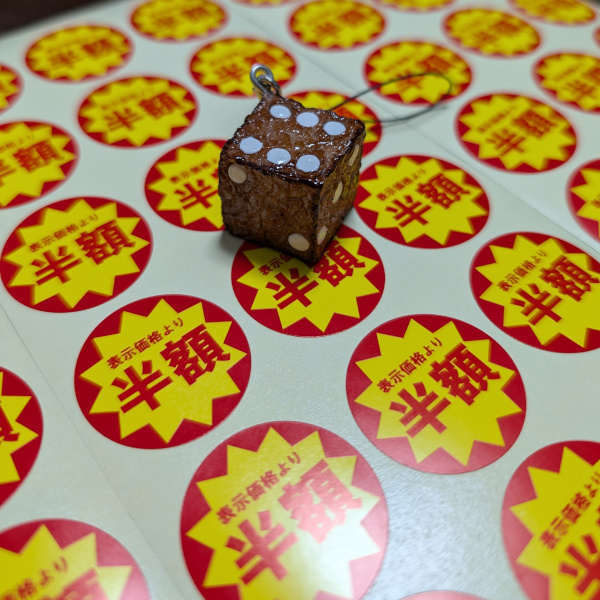 半額シールを並べた上にサイコロステーキにサイコロの目が振られた食品サンプルを置いた写真